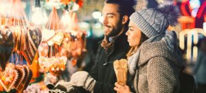 Man and woman looking at a festive stall of food at a market at night. For The Pantiles Christmas Markets for those looking for Festive Events in Tunbridge Wells in Kent