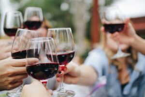 People's hands holding glasses of red wine and clinking for a blog 2024 for a round up of vineyards and wineries in Kent for tours and tastings in the Garden of England