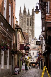 Cobbled street with shops and in the background the outline of Canterbury Cathedral for Top things to do in Canterbury blog post feature. Full of art and culture, events and attractions and ideas and inspiration for visiting Canterbury in Kent