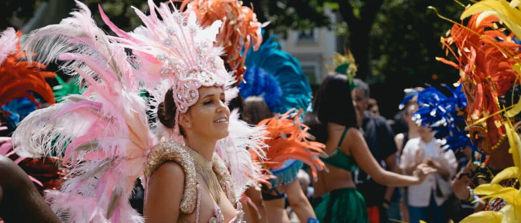 A woman in a feathered headdress with flumes of feathers and people around for Carnival image for Carnvials, country shows and Fayres in Kent guide on www.seekent.co.uk, the ultimate guide to what's on and things to do and see in Kent