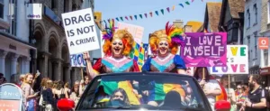 Drag artists in a car driving on street wtih people watching. For Pride Canterbury in Kent listings for the Pride in Kent Guide