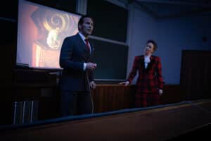 Man standing on front of a projection screen with a woman standing to the side. for New film releases for cinemas in Kent and The Conjuring- Last Rites from Warner Bros.