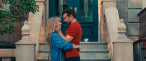 A man and a woman her in a blue shirt he is in a red T-shirt outside building steps. They are cuddling each other facing each other and he cupping her face with his hands. For New film releases for cinemas in Kent and A Big Bold Beautiful Story from Sony Pictures