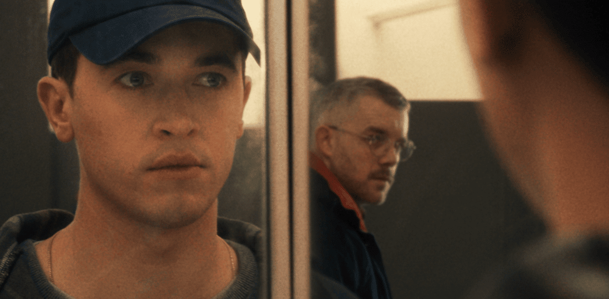 A man in a cap looking at reflection that includes a man in glasses looking back at him For new film releases for cinemas in Kent and Plainclothes from Curzon