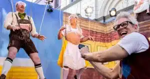 Tow characters dressed in German costume like puppets with a man laughing in front. For new film Jackass The Best and Last