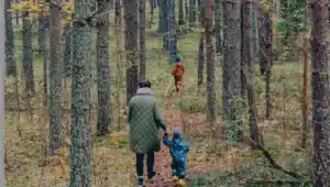 Adult holding hand of young child and another child further ahead in woods for Adult and two children in woods by Siim Lukka at unsplash for 30 Things To Do in Kent for October Half Term guide